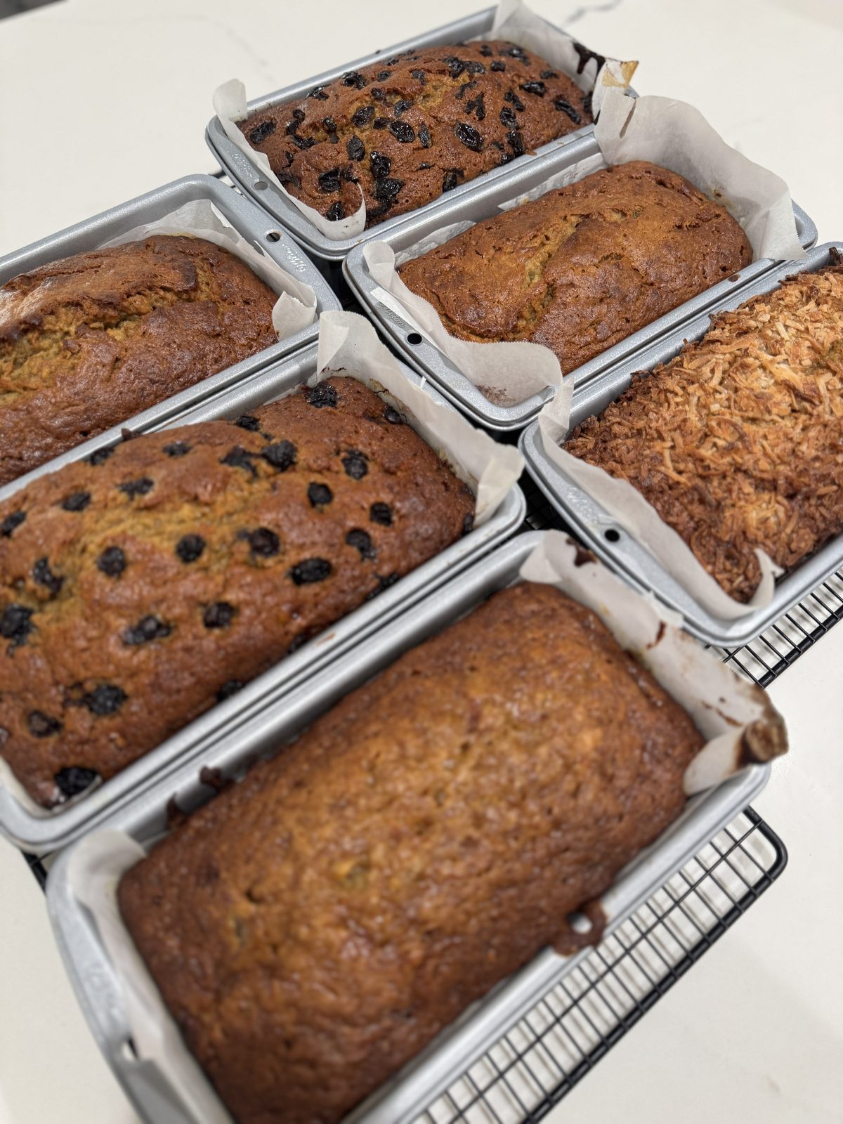 Multiple seasonal banana bread flavors lined up, including chocolate chip, coconut butterscotch, and classic